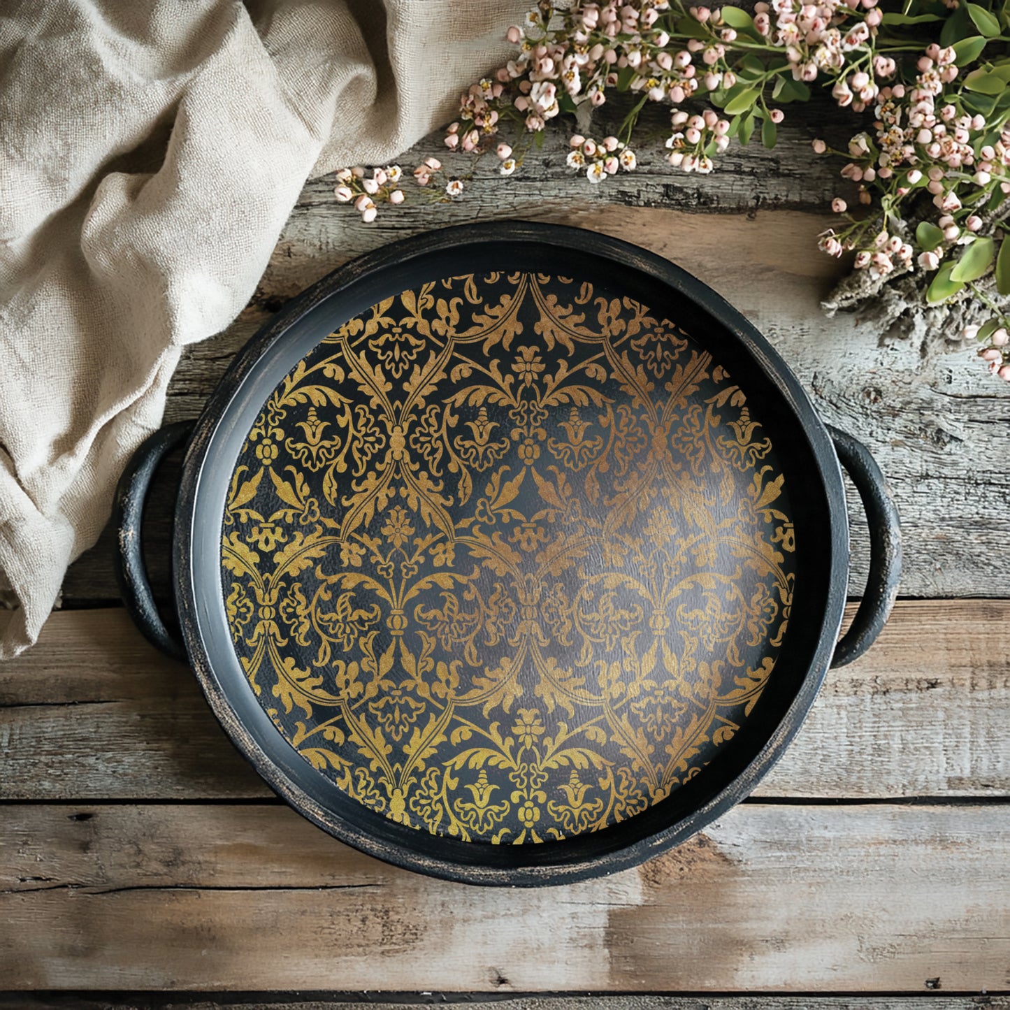 Decorative black tray, with gold patterns from the Emporium transfer, on a wooden surface with flowers and fabric.