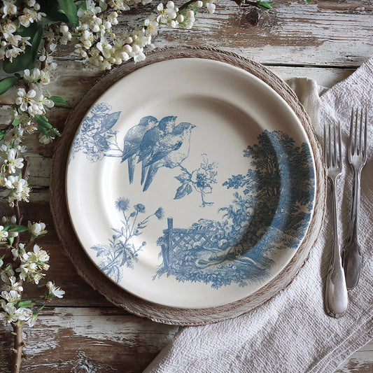 Decorative stamped plate with blue meadowlark design on a rustic wooden table with flowers and cutlery.