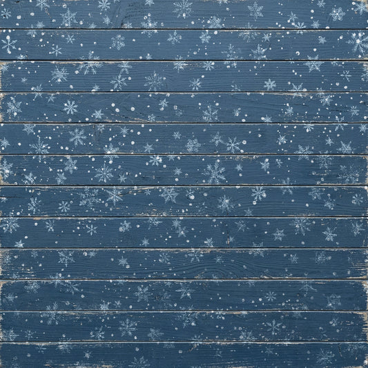A square decorative panel or backdrop featuring a distressed blue wood plank design with scattered white snowflake stampings and snowflurries across the surface.