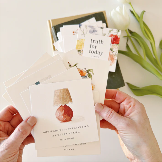 Hands holding a card with a lamp illustration and text, with more cards and tulips in the background.
