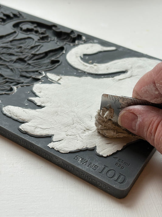 A hand using a flat edge to smooth air dry clay into the Swans mould.