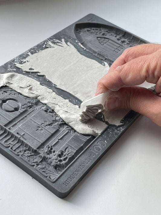 A hand scraping air dry clay across the Hidden Hollow mould.