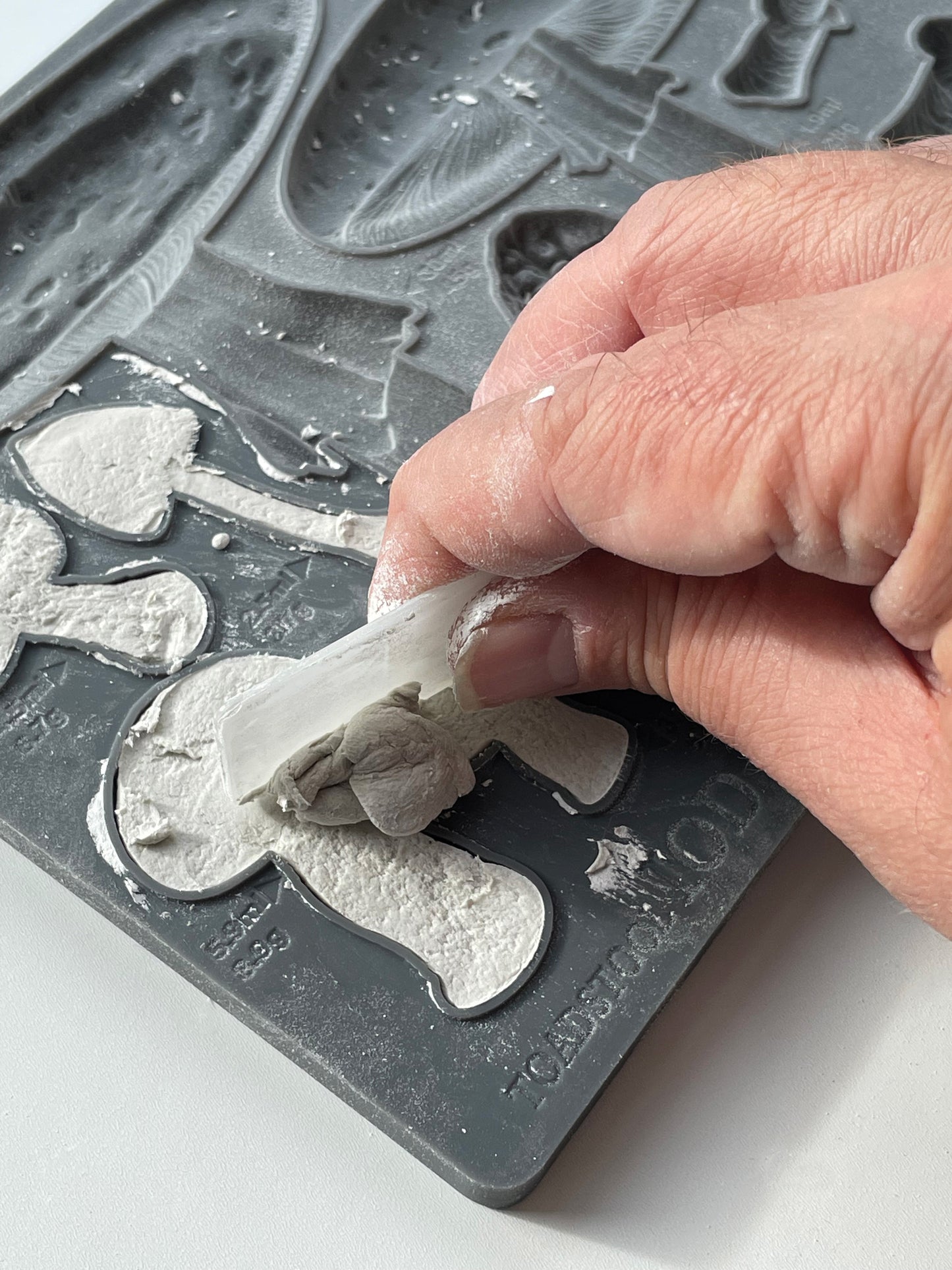 A hand using a plastic scraper to level out their clay on the IOD Toadstool mould
