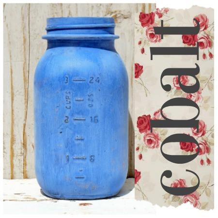 A jar labeled 'Cobalt' by Sweet Pickins Milk Paint, displaying a blue painted finish on a wooden surface with a floral patterned fabric in the background.