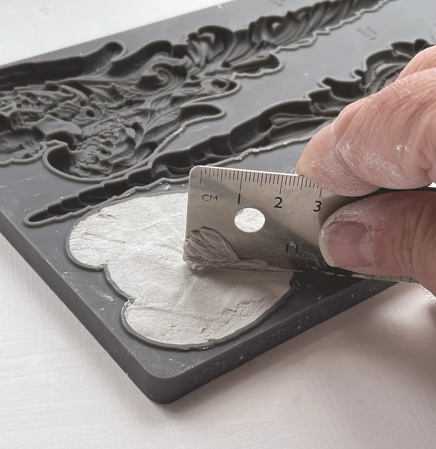 A hand using a straight edge to smooth over clay in a Silicone Mould.