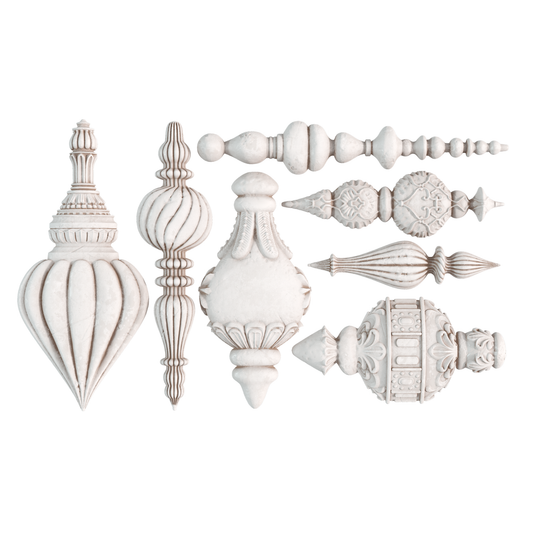 A set of ornate white clay castings arranged on a plain white background, including pointed, ribbed, fluted, and carved ornament styles.