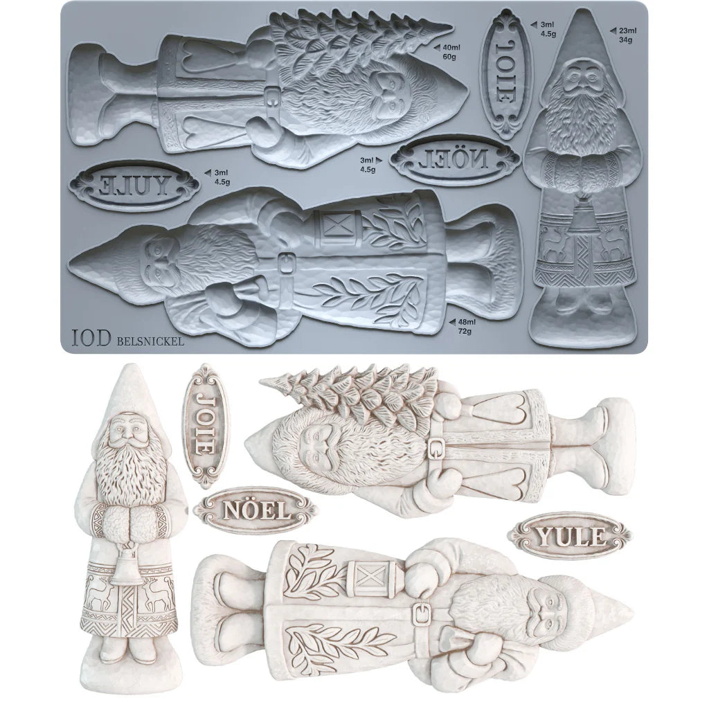 A mold-making product display showing a gray rectangular mold tray with Christmas-themed cavities and several light off-white sculpted figurines and labels above it, including a gnome, a fish, a tree, and words such as JOY, NOÉL, and YULE.