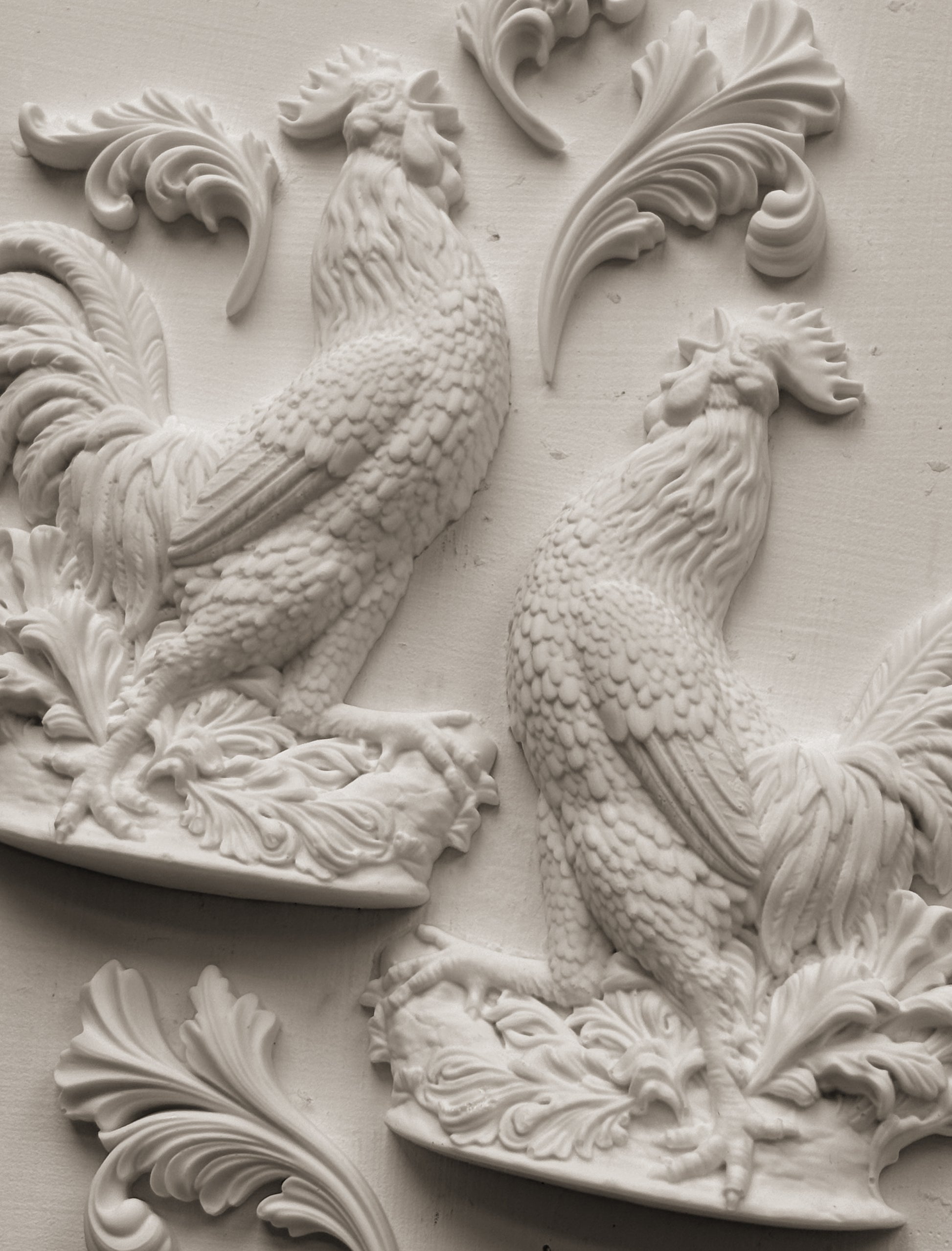 Decorative relief of two roosters with intricate patterns on a light gray background
