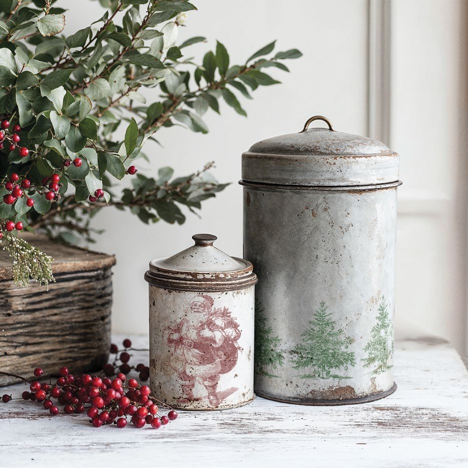 Vintage-style metal canisters with decorative lids on a wooden surface with greenery and berries, stamped using the "Christmas Wishes" stamp from "IOD"