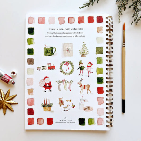 Back cover of Emily Lex 'Christmas' Workbook with 12 green and red holiday illustrations and a watercolor brush sitting next to the workbook, both on a table.