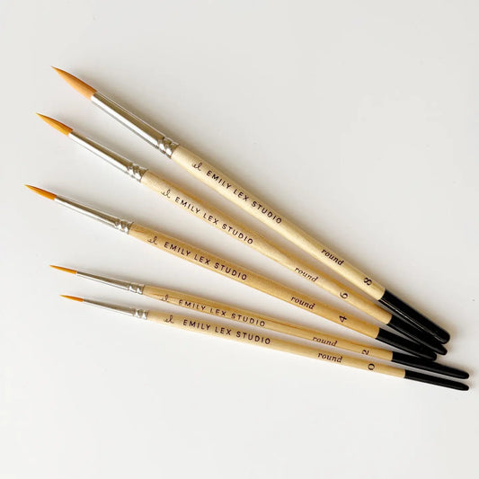 5 watercolor brushes engraved with "Emily Lex Studio" sitting on a table at diagonal angle.