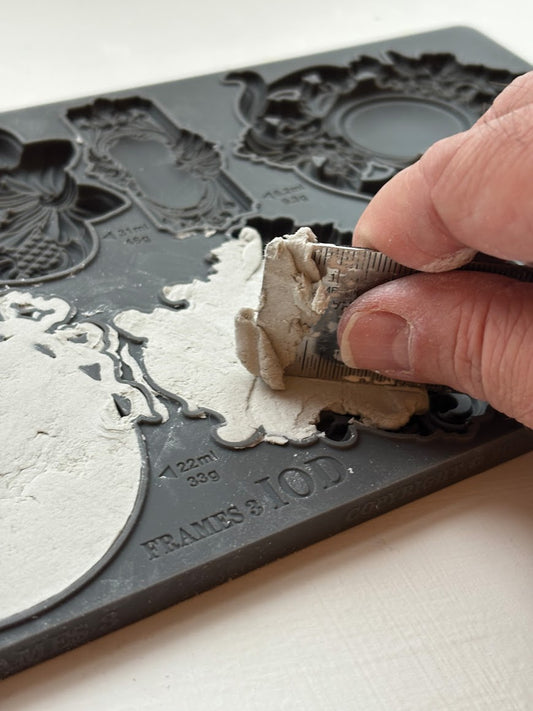 Hand using a straight edge to fit air dry clay into “Frames 3 IOD” mould.