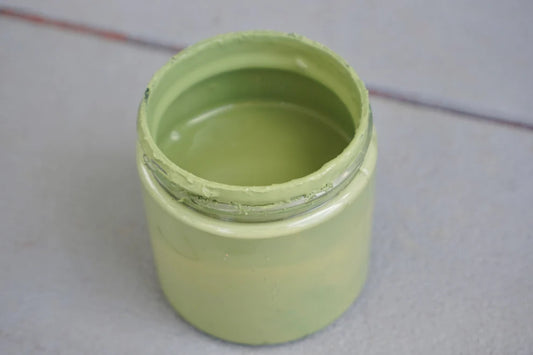 An unlabeled jar of sage colored green paint sitting on a grey table.