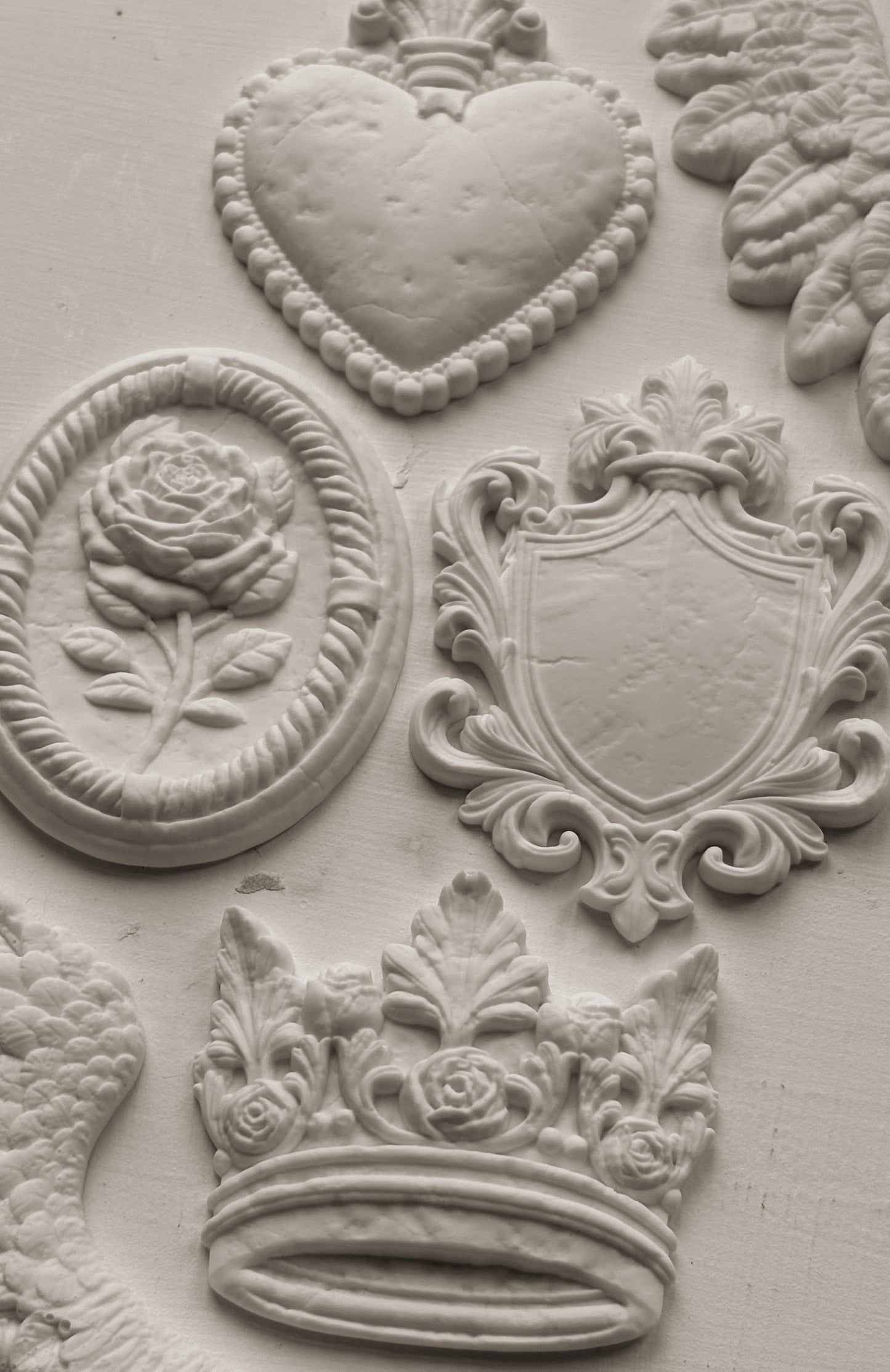 Decorative clay-cast elements including a heart, rose, shield, and crown on a textured surface.