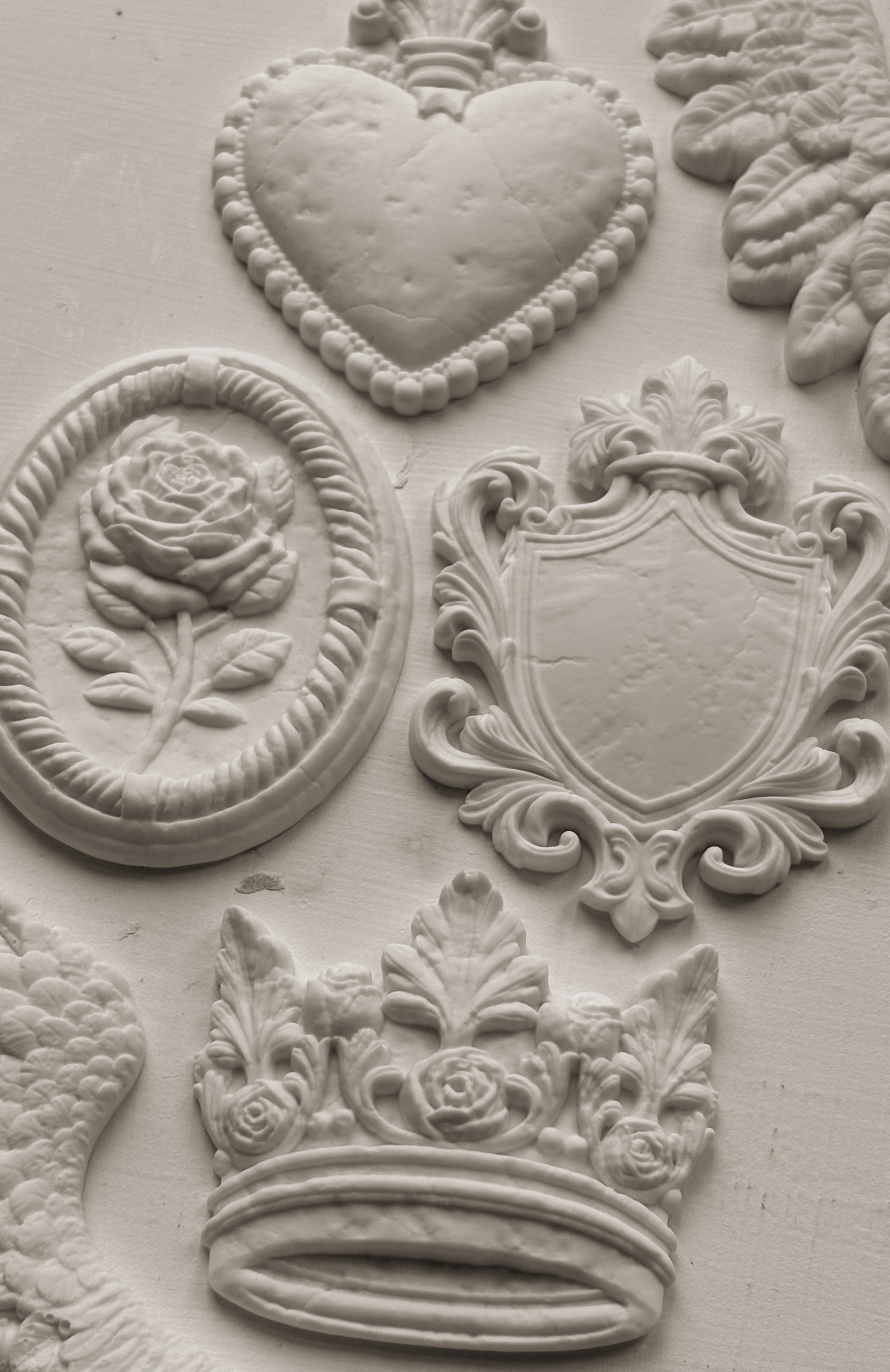 Decorative clay-cast elements including a heart, rose, shield, and crown on a textured surface.