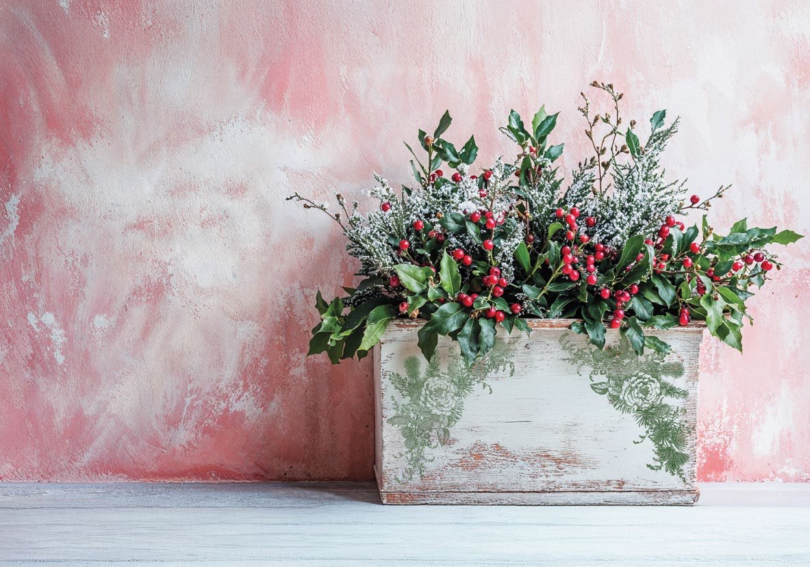 Decorative floral arrangement with red berries in a wooden box, stamped with the "Holly & Pine" stamp from "IOD", placed against a pink and white textured background