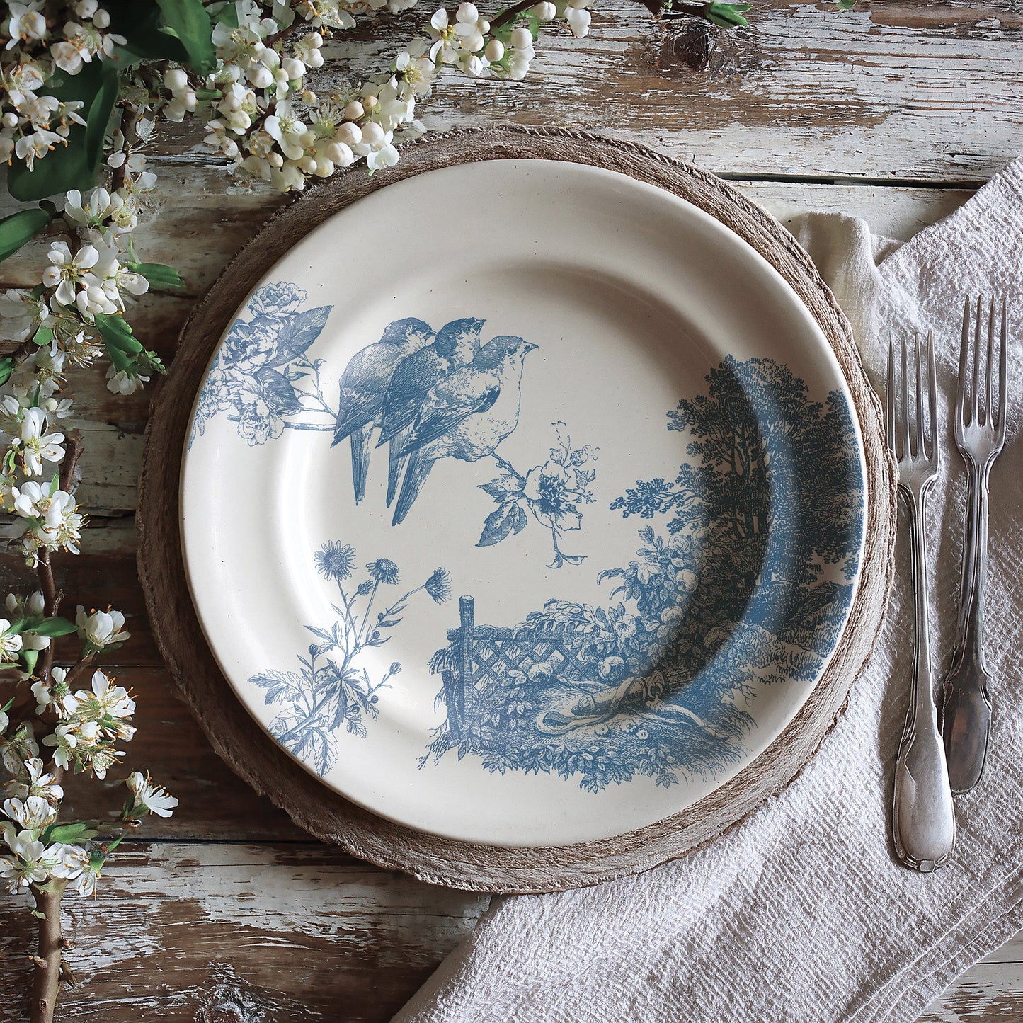 Decorative stamped plate with blue meadowlark design on a rustic wooden table with flowers and cutlery.