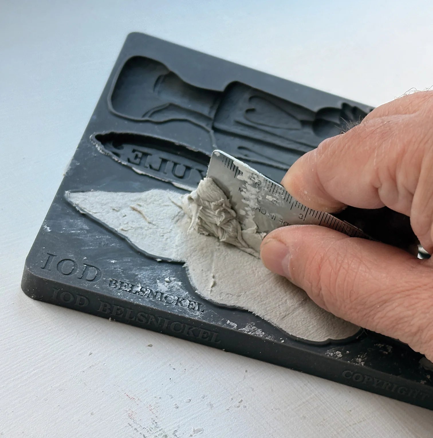 A close-up of a hand using a metal spatula to scrape excess air dry clay out of the IOD 'Belsnickel' mould.