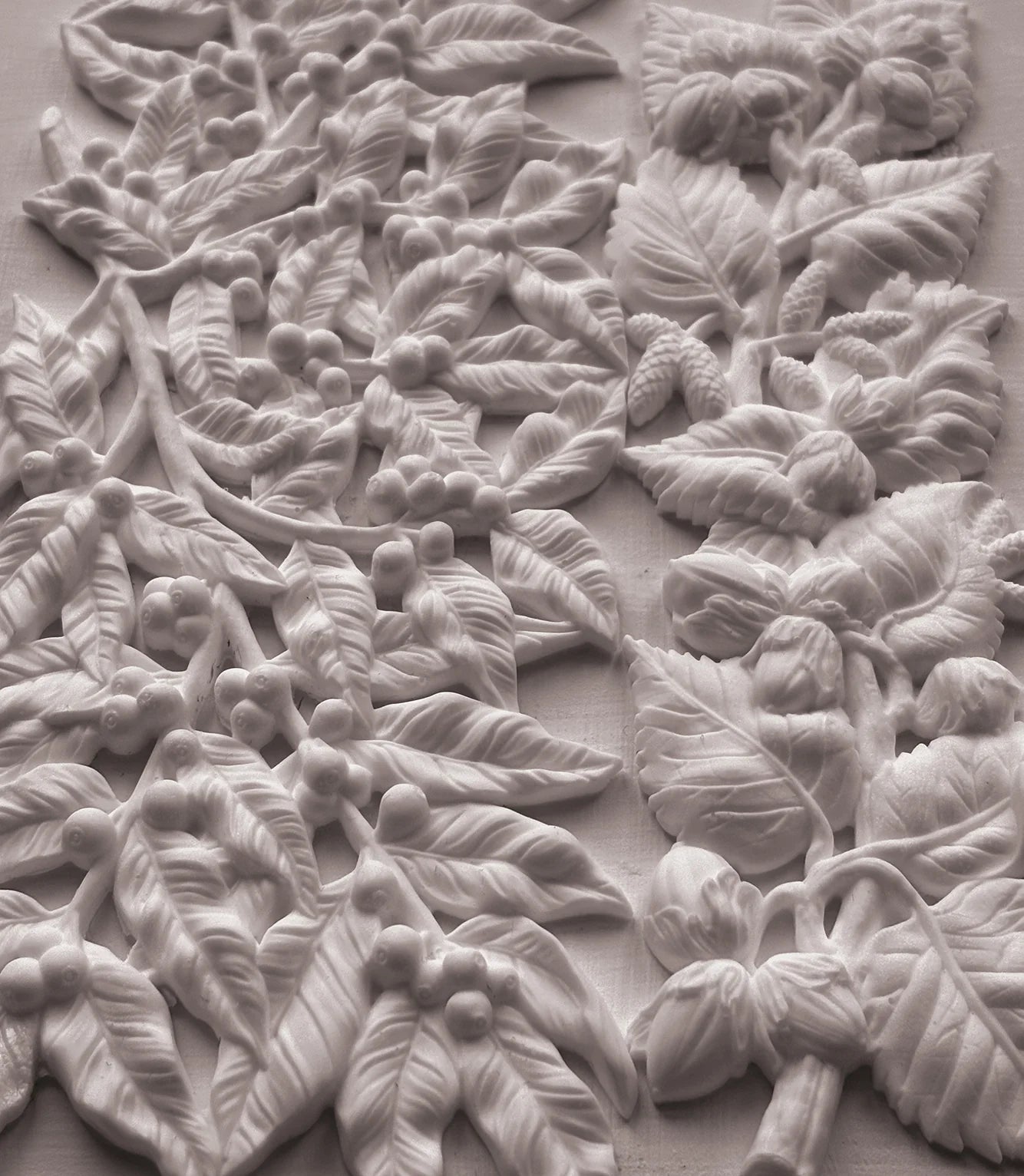 White floral and leaf mould castings with raised botanical details on a light background.