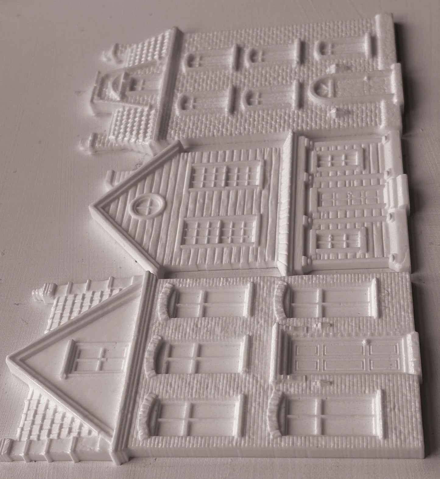 White resin miniature building pieces for DIY crafts, featuring detailed house designs with windows, doors, and textured brick patterns, arranged on a light gray background.