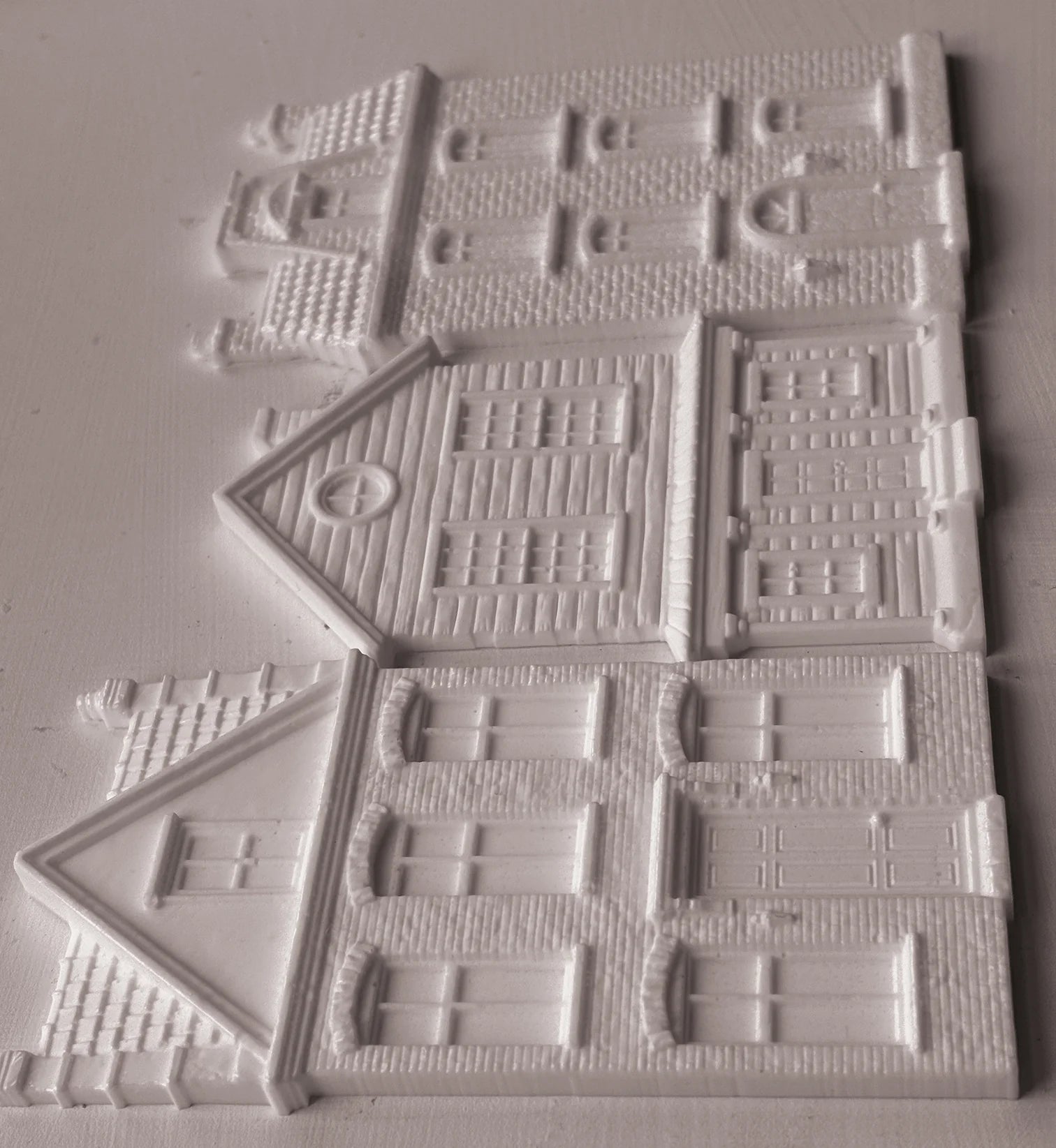 White resin miniature building pieces for DIY crafts, featuring detailed house designs with windows, doors, and textured brick patterns, arranged on a light gray background.