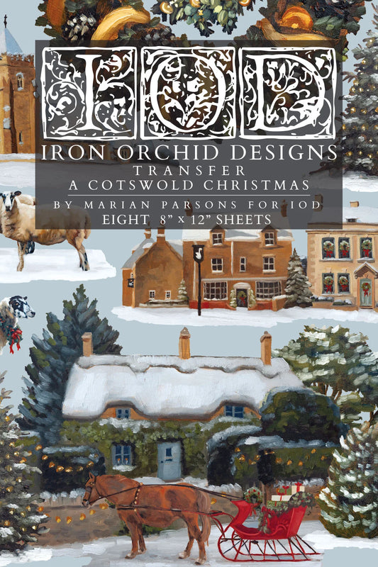Cover of Transfer: 'A Cotswold Christmas' by Marian Parsons, featuring an illustrated winter village scene with snow-covered cottages, evergreen trees, a horse-drawn sleigh, and a large decorative 'IOD' monogram at the top.