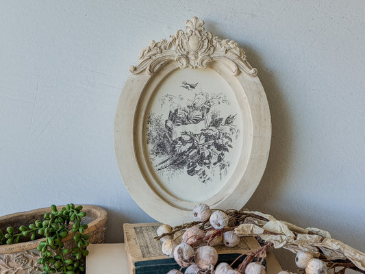 Decorative oval frame with floral stamped design from the Little Lark Inlay, on a light blue wall