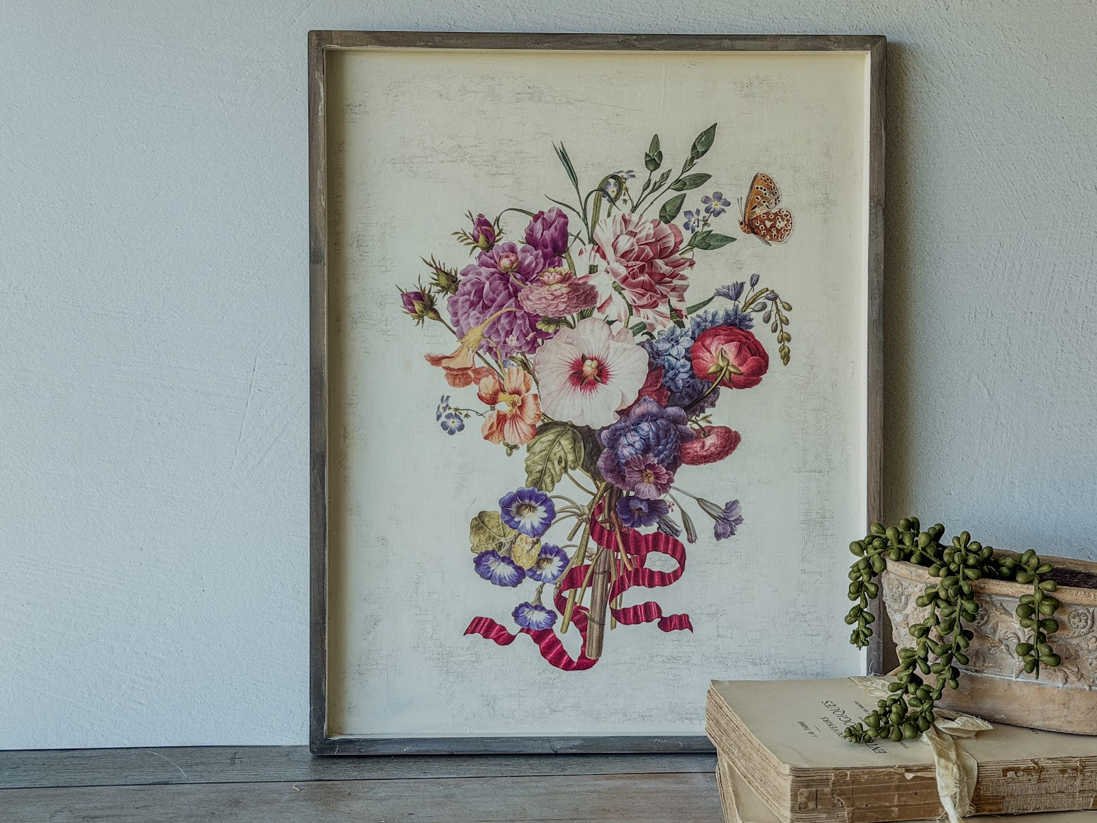 Floral print from the Marché des Fleurs transfer in a wooden frame on a wall with a rustic wooden table and plants.