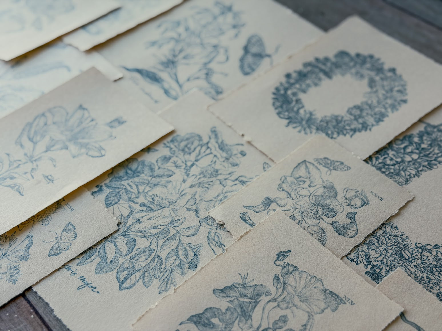 Collection of blue floral and leaf stamped designs on beige paper sheets.