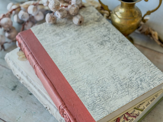 Vintage book with a red binding on a wooden surface with a stamped cover in a map design.