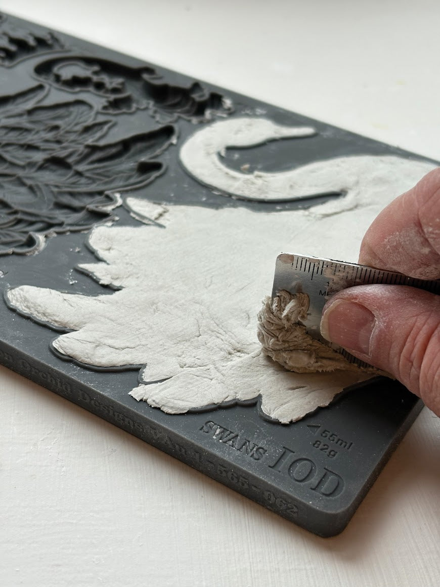 A hand using a flat edge to smooth air dry clay into the Swans mould.