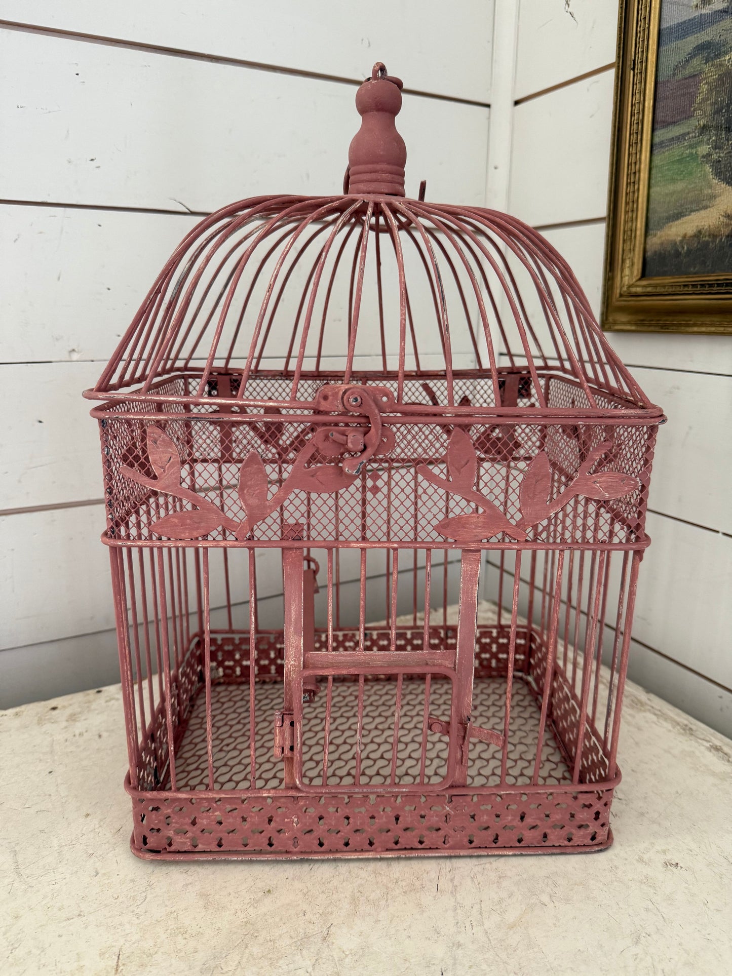A vintage bird cage painted with milk paint from "Sweet PIckins Milk Paint Co." in the shade Trellis Rose, up against a white paneled background.