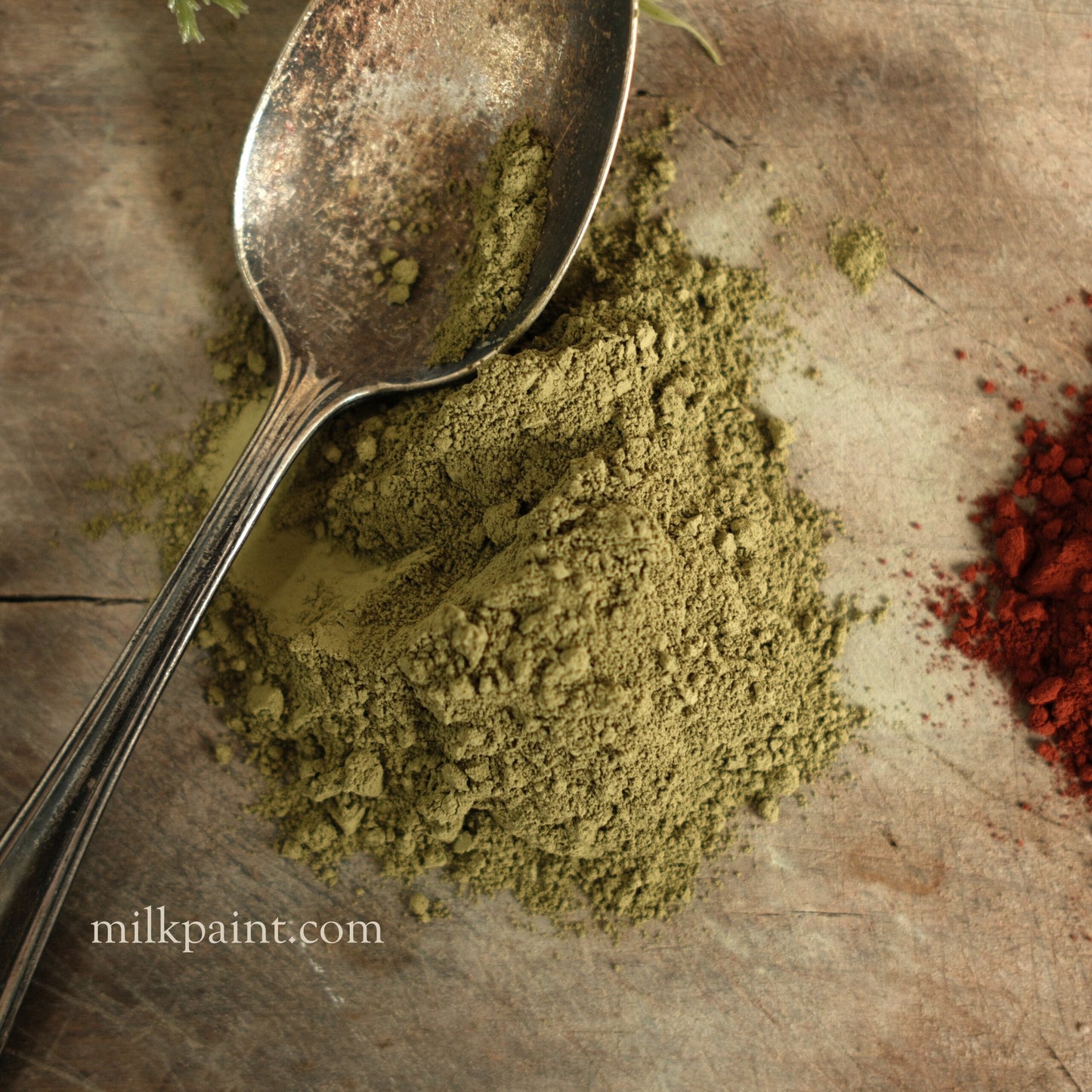 Green powder with a spoon on a rustic surface, featuring the brand 'milkpaint.com'.