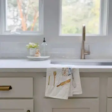 Kitchen counter with a baking towel featuring kitchen utensils, sink, and window view.