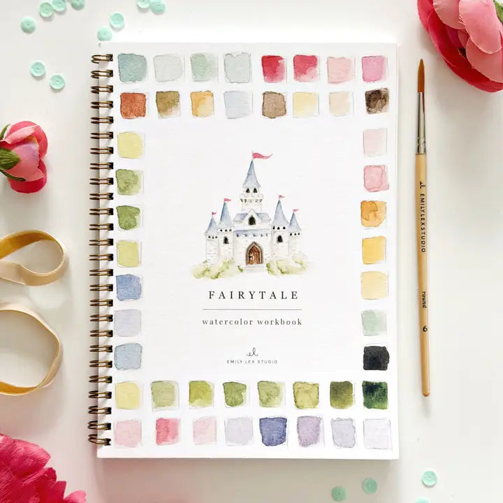 Fairytale watercolor workbook with a castle illustration on a white surface with flowers and a brush.