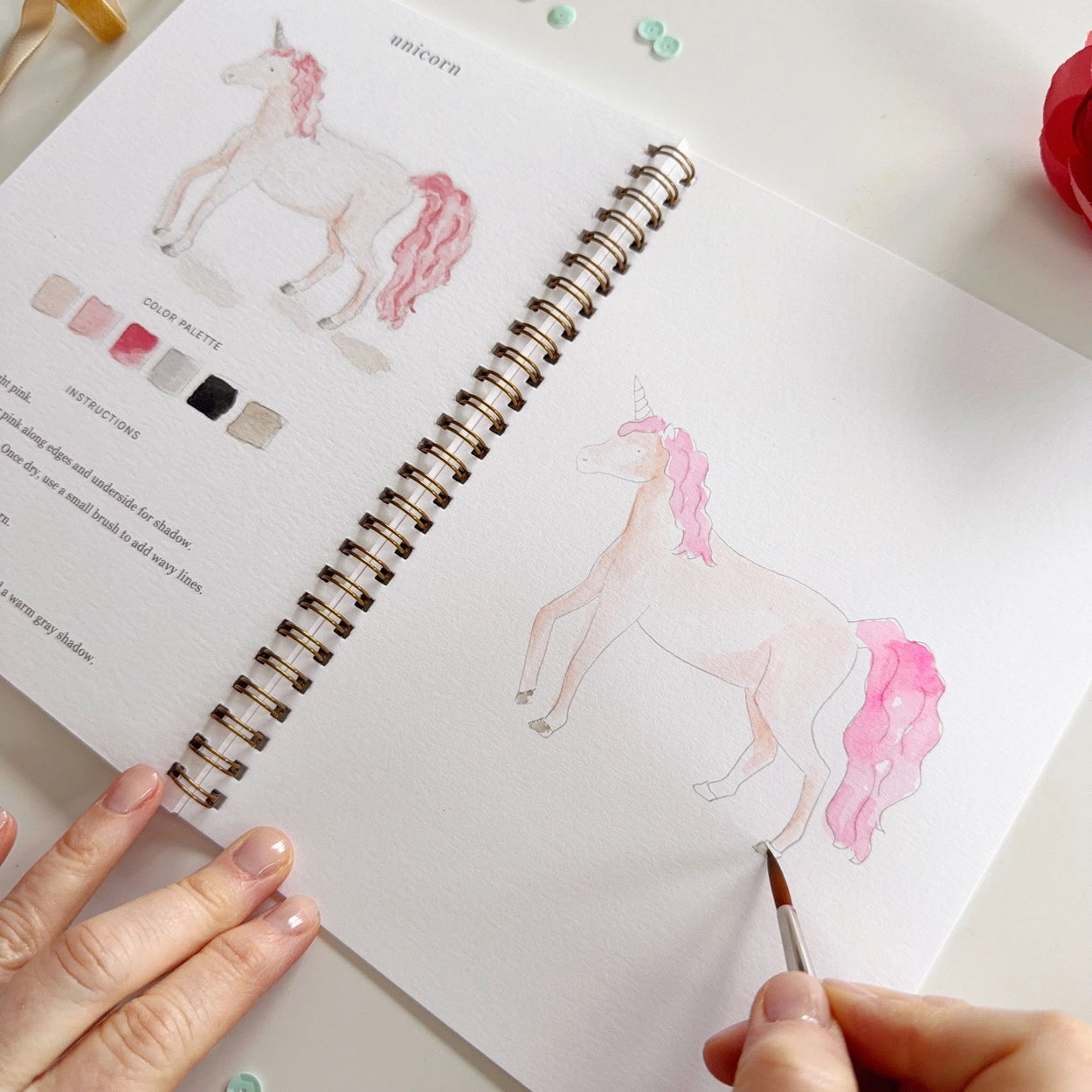 Person watercolor painting a unicorn in a workbook.