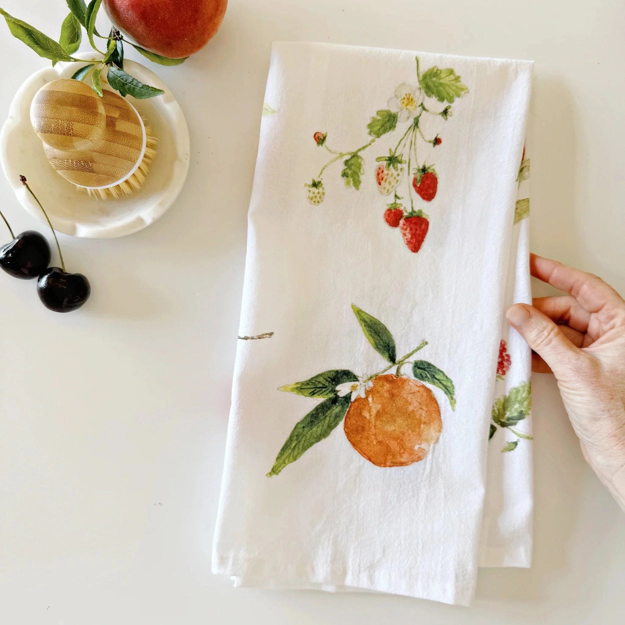 Hand holding a towel with fruit design on a white surface