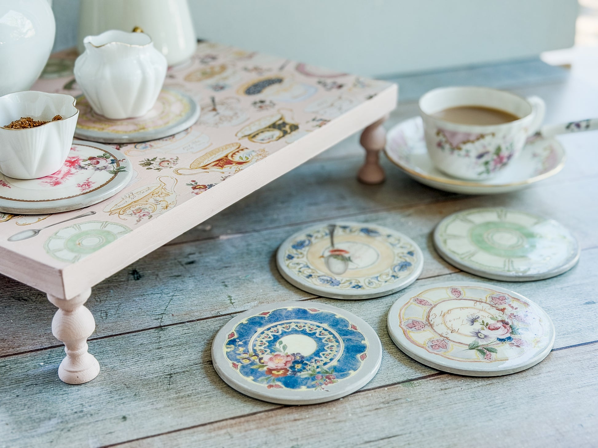 Decorative coasters with floral patterns on a wooden surface with a teapot and cups, created using the IOD Belgravia transfer.