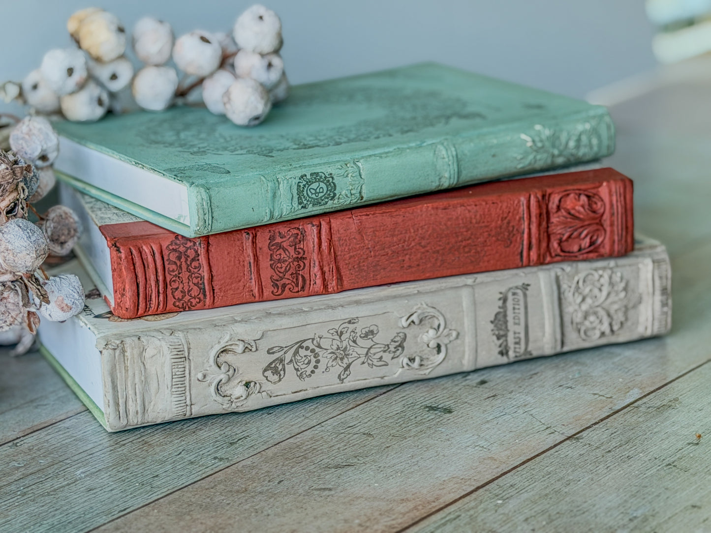 Three stacked book spines, created using the Bookish Mould, each colored and stamped and on a wood table.