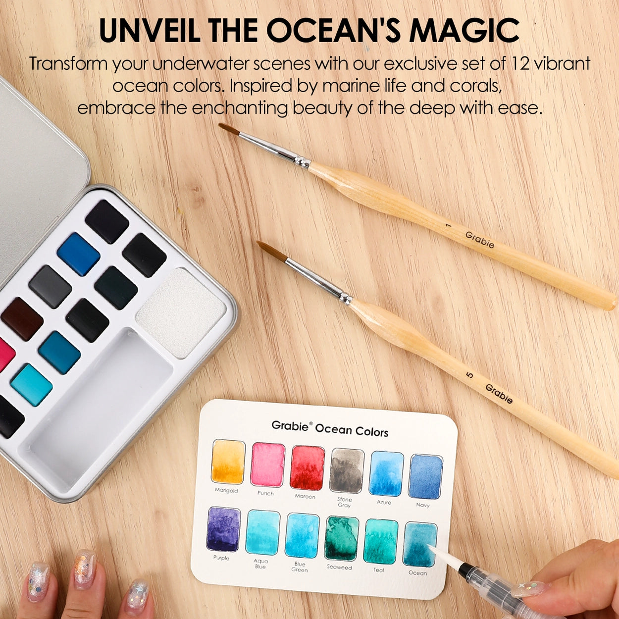 Set of watercolor paints with brushes on a wooden surface, featuring ocean-themed colors.