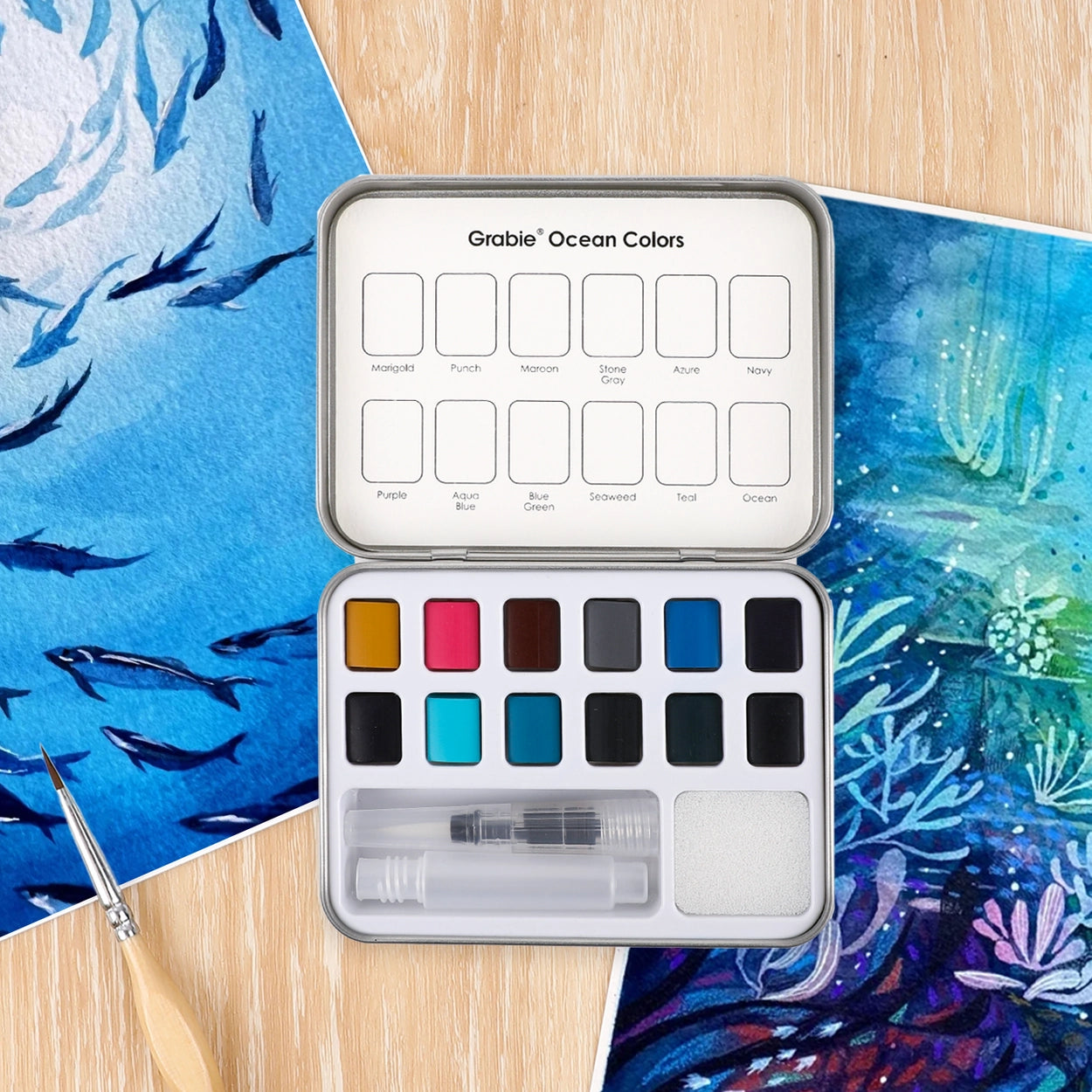 Watercolor paint set with ocean-themed colors on a wooden surface with watercolor paintings.