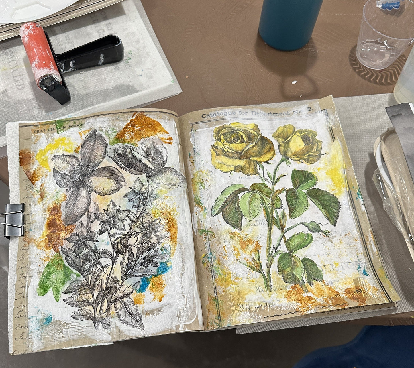 Open journal with floral illustrations on a table with art supplies.