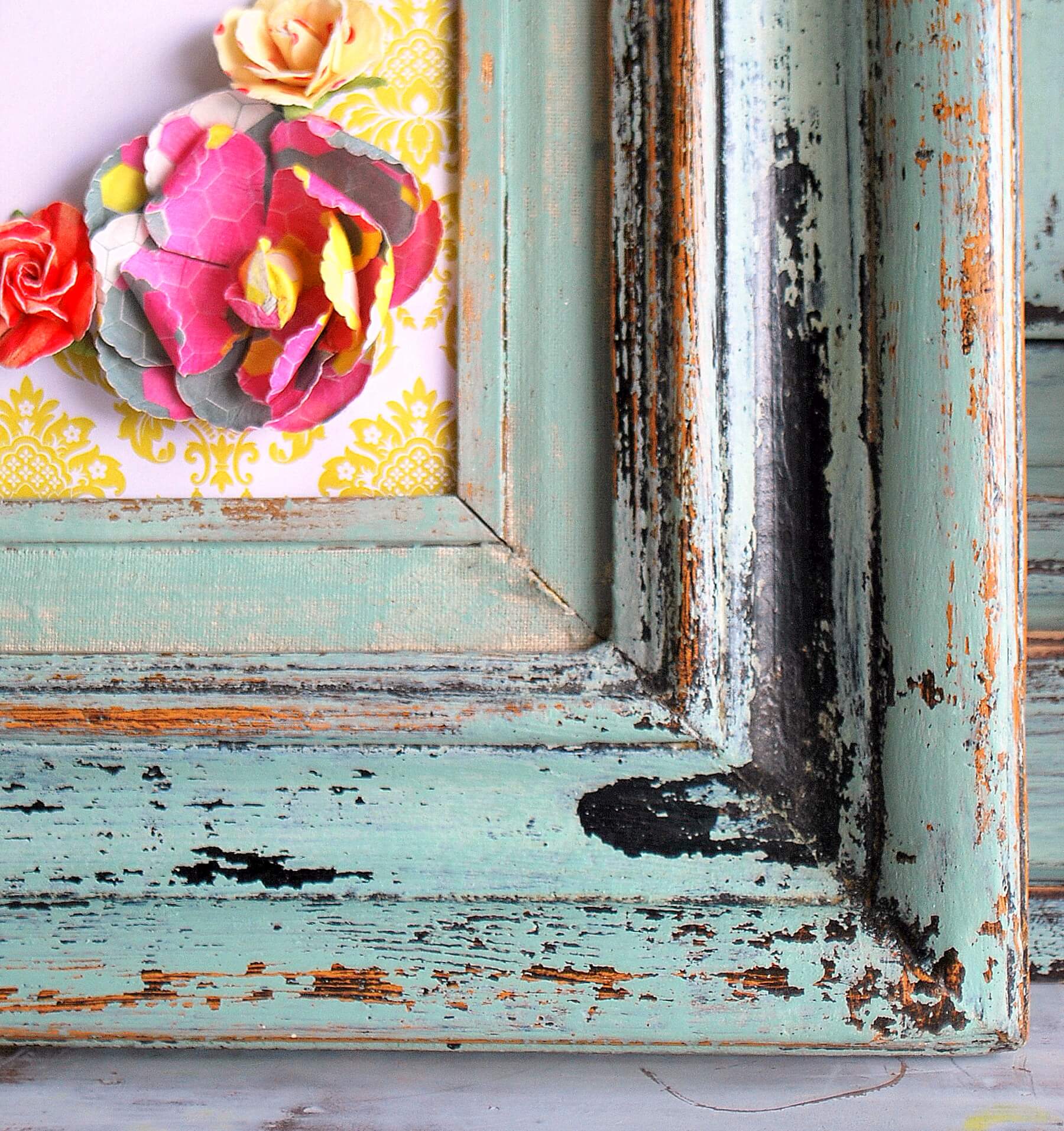 The corner of a distressed frame that is painted in milk paint in the shade "Sweetie Jane".