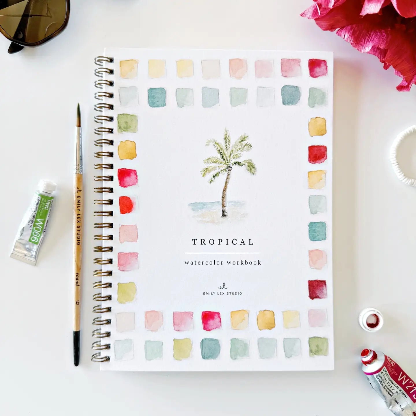 Front cover of a Tropical watercolor workbook with a paintbrush and paint tube on a white surface