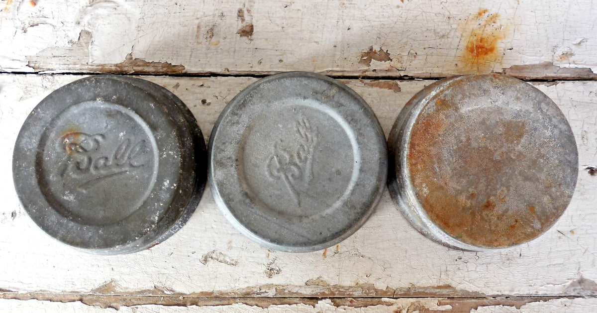 Three milk-painted metal lids with 'Ball' branding on a rustic wooden surface.
