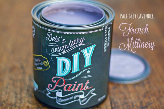 An open can of purple paint in the color "French Millinery" sitting on a wooden table.