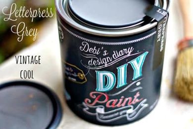 A can of DIY Paint in Letterpress Gray color, with a black label featuring white and blue text. A paintbrush and a wooden object are visible in the background.