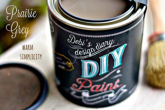 A can of Prairie Grey DIY paint with a brush and a cup of paint, showcasing the product with a decorative text on the can.
