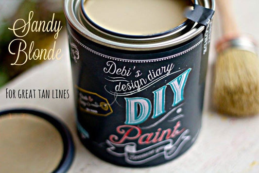 A can of Sandy Blonde DIY paint with a brush, indicating the paint is intended for great tan lines and designing with a DIY style.