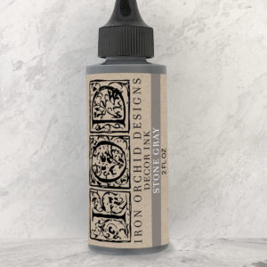 An unopened 2 oz. bottle of IOD Decor ink in the color "Stone Gray", with bottle against a white wall.